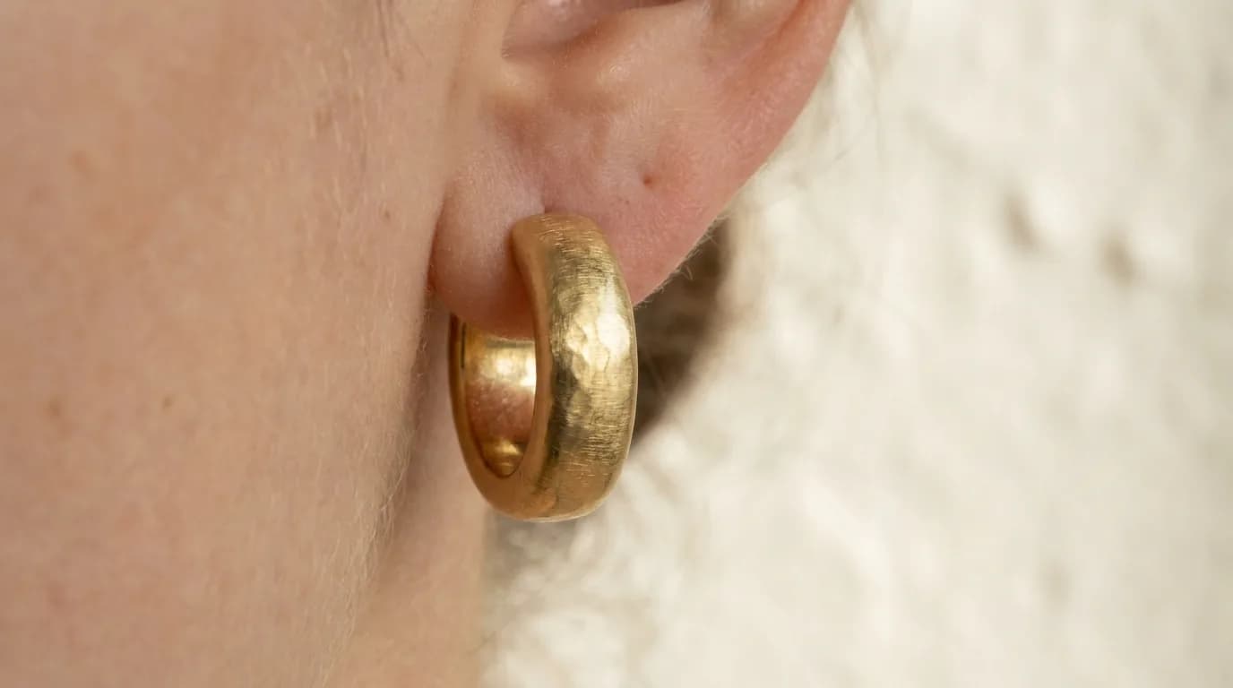 A gold-tone hoop earring worn close up against a light background